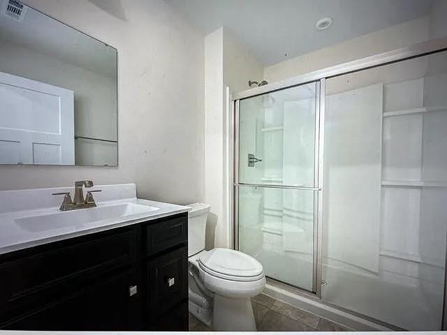 bathroom featuring tile patterned floors, an enclosed shower, vanity, and toilet