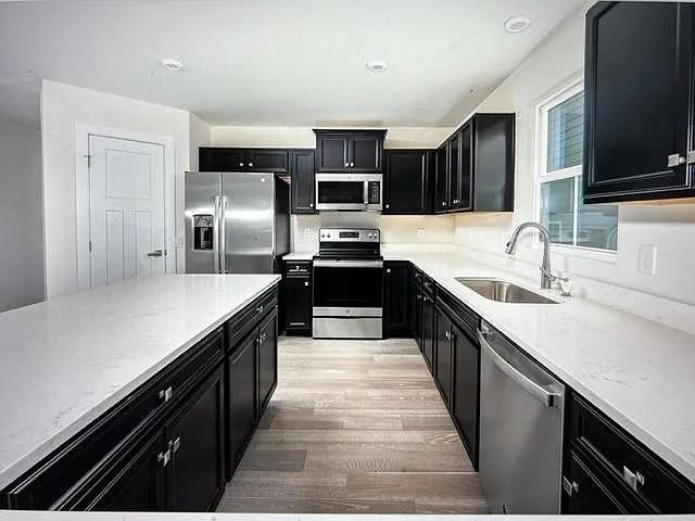 kitchen with light stone countertops, sink, appliances with stainless steel finishes, and light wood-type flooring