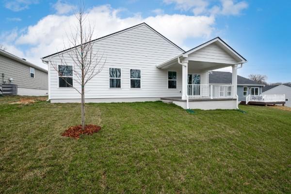 rear view of property featuring a lawn, central AC unit, and covered porch