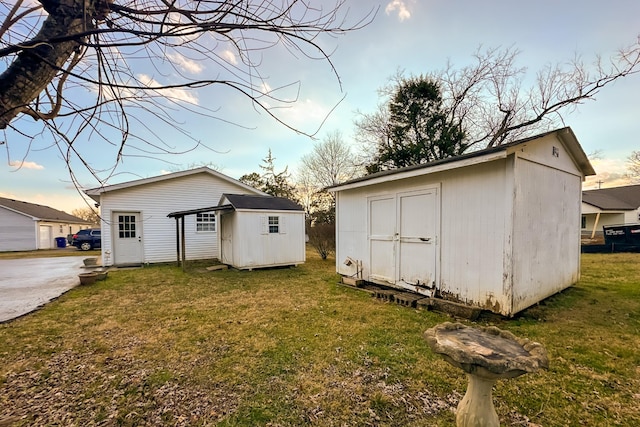 back house at dusk featuring a yard and a storage unit