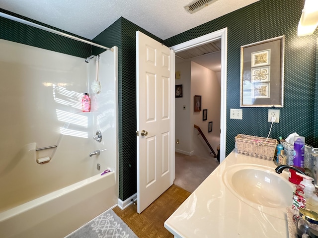 bathroom with a textured ceiling, washtub / shower combination, parquet floors, and vanity