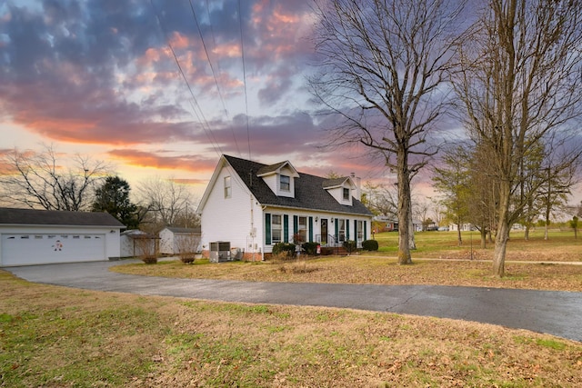 cape cod home with a garage, a lawn, cooling unit, and an outdoor structure