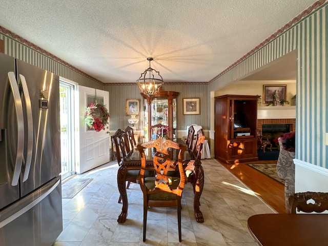 dining area featuring a textured ceiling, a notable chandelier, a brick fireplace, and ornamental molding