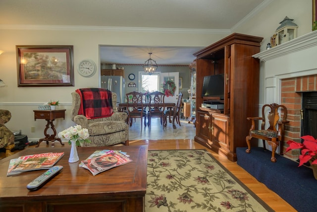 living room with a brick fireplace, ornamental molding, light hardwood / wood-style floors, and an inviting chandelier