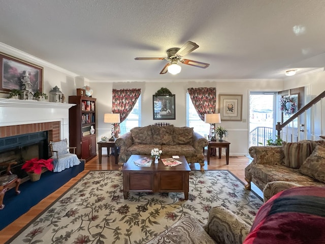 living room featuring a textured ceiling, a fireplace, light hardwood / wood-style floors, ceiling fan, and crown molding