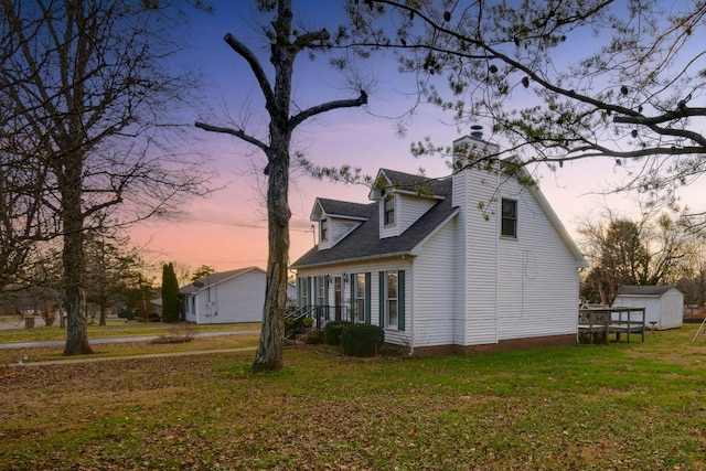 property exterior at dusk featuring a lawn and a storage unit