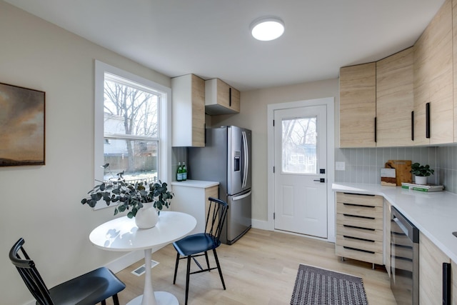 kitchen with light brown cabinets, wine cooler, decorative backsplash, stainless steel fridge, and light hardwood / wood-style flooring