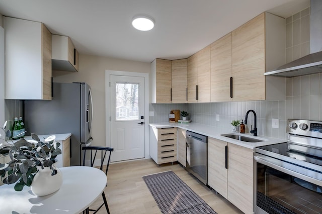 kitchen featuring wall chimney range hood, light hardwood / wood-style floors, sink, appliances with stainless steel finishes, and light brown cabinets