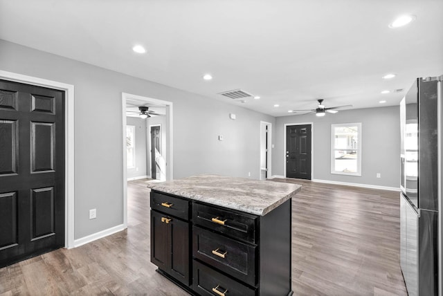 kitchen with light hardwood / wood-style floors, stainless steel fridge, ceiling fan, a kitchen island, and light stone counters