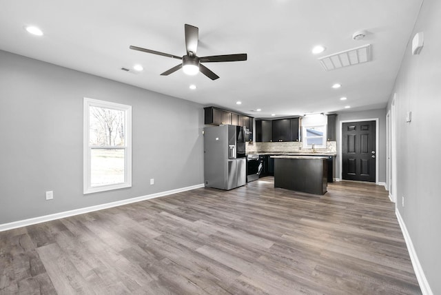 kitchen featuring ceiling fan, a kitchen island, decorative backsplash, dark hardwood / wood-style flooring, and stainless steel fridge