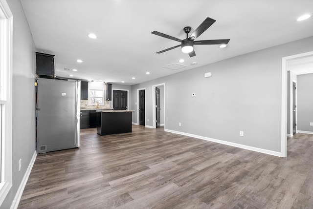 kitchen featuring ceiling fan, tasteful backsplash, a center island, stainless steel refrigerator, and dark wood-type flooring