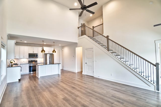 kitchen featuring a high ceiling, pendant lighting, white cabinets, appliances with stainless steel finishes, and wood-type flooring