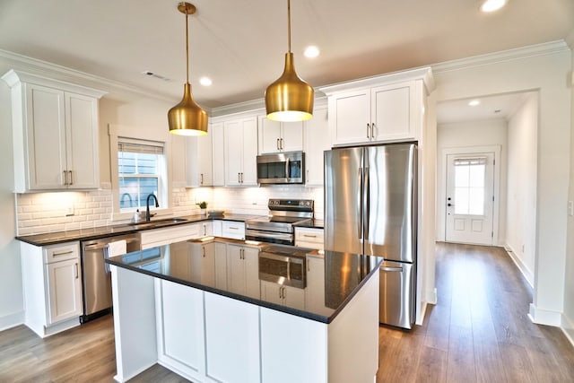 kitchen with pendant lighting, a kitchen island, white cabinetry, stainless steel appliances, and sink