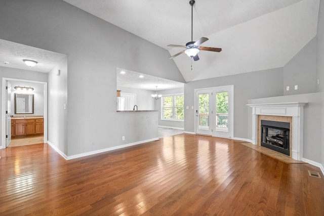 unfurnished living room featuring ceiling fan with notable chandelier, light hardwood / wood-style floors, lofted ceiling, and a fireplace