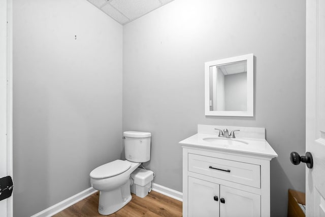 bathroom featuring wood-type flooring, toilet, vanity, and a paneled ceiling