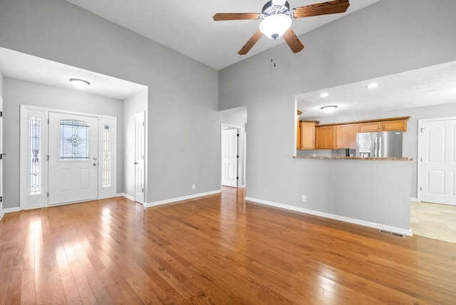 unfurnished living room featuring high vaulted ceiling, a textured ceiling, light hardwood / wood-style flooring, and ceiling fan