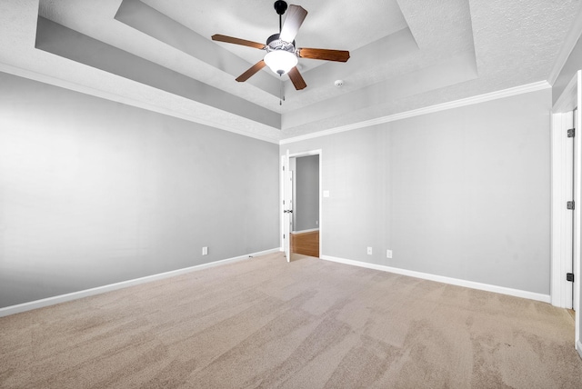 carpeted empty room with a raised ceiling, ceiling fan, crown molding, and a textured ceiling