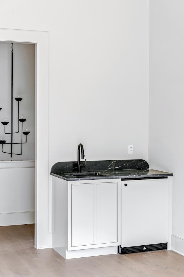 bar with white cabinets, sink, fridge, and dark stone counters