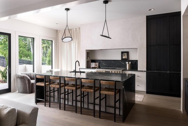 kitchen featuring pendant lighting, white cabinets, an island with sink, decorative backsplash, and a breakfast bar