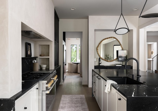 kitchen with high end stainless steel range, dark stone counters, pendant lighting, white cabinets, and sink