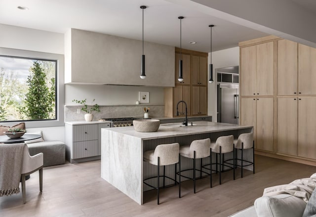 kitchen featuring a kitchen bar, a center island with sink, light wood-type flooring, built in fridge, and pendant lighting