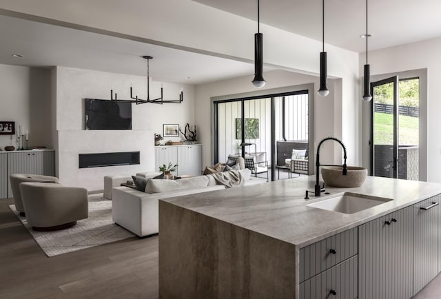 kitchen featuring pendant lighting, sink, a kitchen island with sink, light stone counters, and light hardwood / wood-style flooring