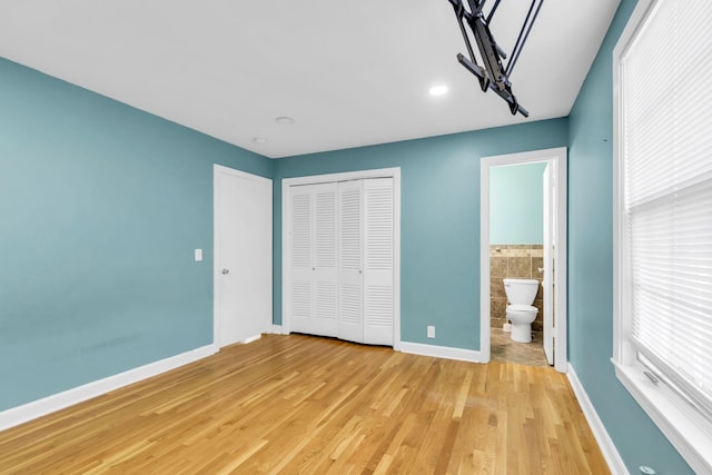 unfurnished bedroom with connected bathroom, light hardwood / wood-style flooring, a closet, and tile walls