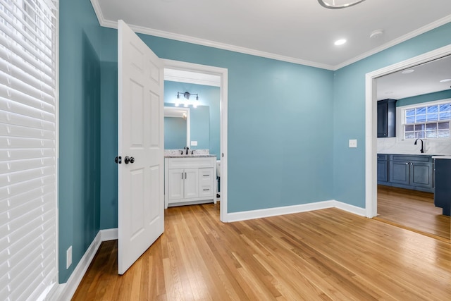 unfurnished bedroom with sink, connected bathroom, ornamental molding, and light wood-type flooring