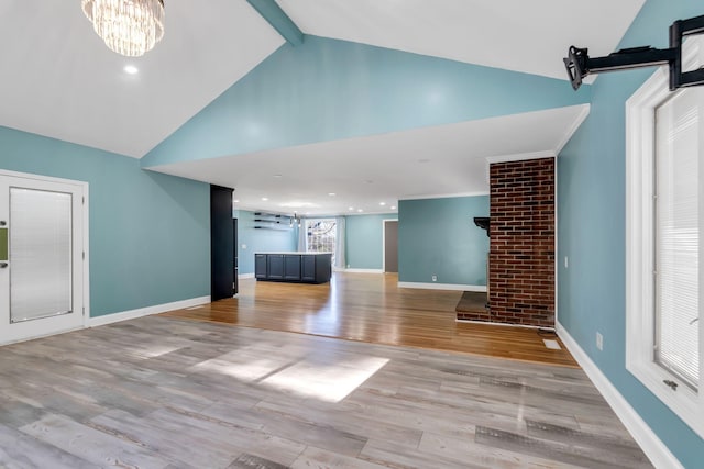 unfurnished living room with light wood-type flooring, an inviting chandelier, and vaulted ceiling with beams