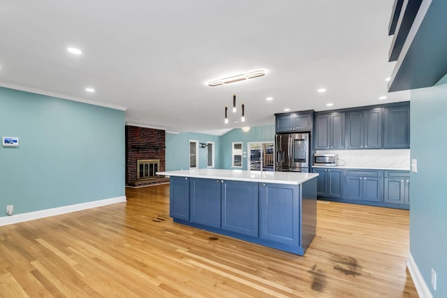 kitchen with pendant lighting, appliances with stainless steel finishes, a kitchen island with sink, and light wood-type flooring