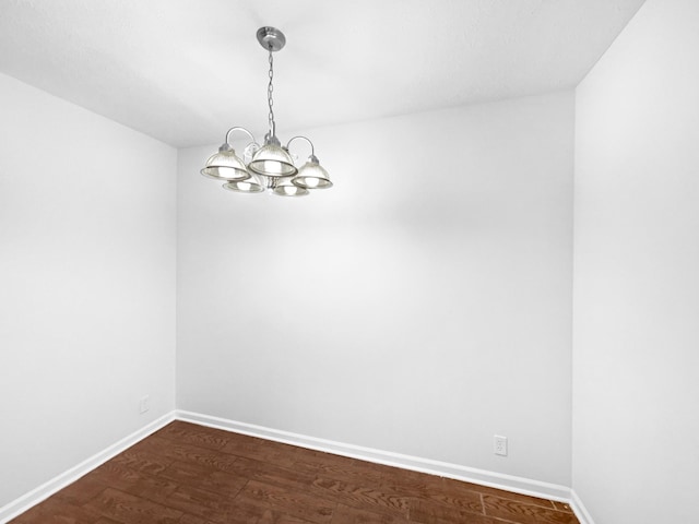 unfurnished room featuring an inviting chandelier and dark wood-type flooring