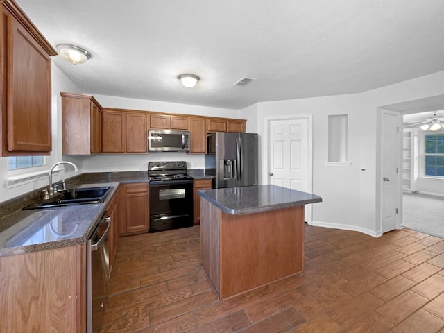 kitchen with appliances with stainless steel finishes, a center island, dark hardwood / wood-style flooring, dark stone counters, and sink