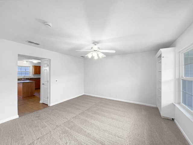 empty room featuring sink, a healthy amount of sunlight, light colored carpet, and ceiling fan