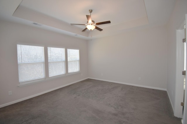 carpeted empty room with ceiling fan, a wealth of natural light, and a tray ceiling
