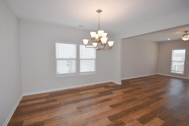unfurnished room with plenty of natural light, ceiling fan with notable chandelier, and dark hardwood / wood-style floors