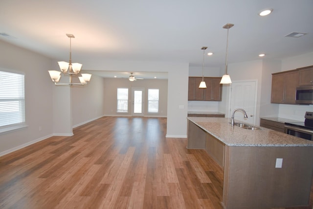 kitchen with light stone countertops, pendant lighting, stainless steel appliances, sink, and a kitchen island with sink