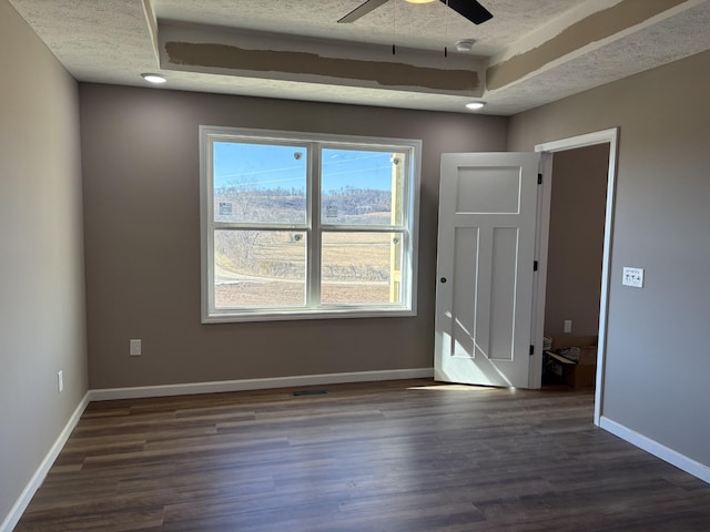 empty room featuring ceiling fan, dark wood-type flooring, a textured ceiling, and a tray ceiling