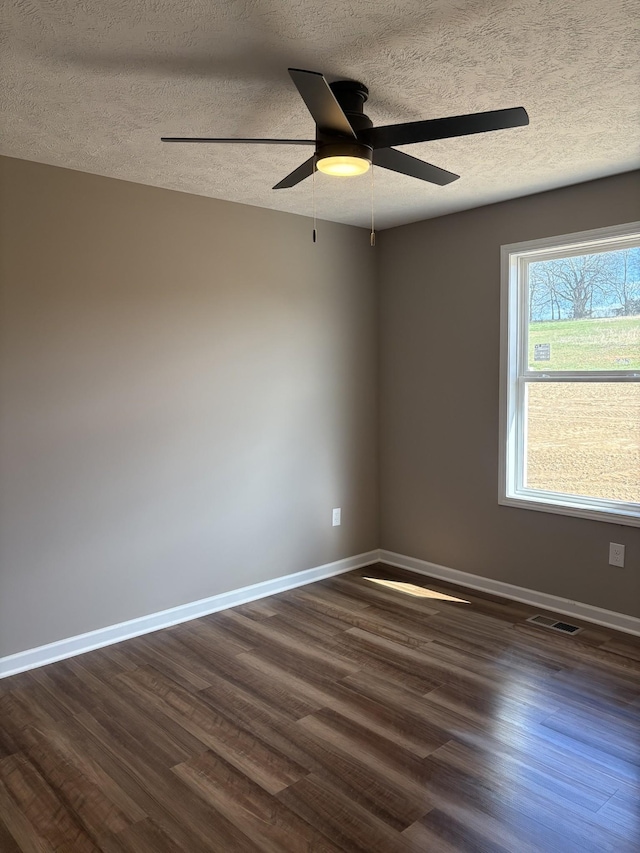 spare room featuring a textured ceiling, ceiling fan, dark wood-type flooring, visible vents, and baseboards