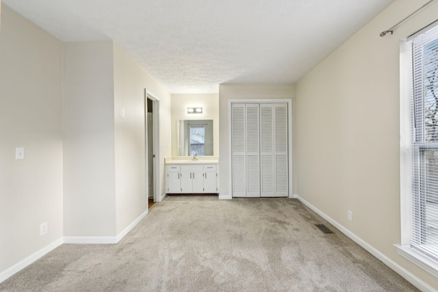 unfurnished bedroom with a closet, sink, light colored carpet, and ensuite bath