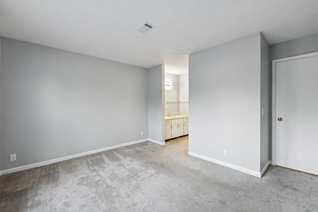 unfurnished bedroom with sink, a textured ceiling, ensuite bathroom, and light carpet