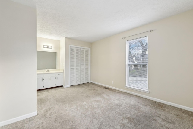 unfurnished bedroom featuring sink, a textured ceiling, ensuite bathroom, and light carpet