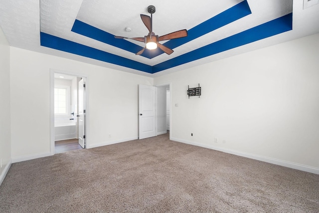 unfurnished bedroom with ceiling fan, carpet floors, a tray ceiling, ensuite bath, and a textured ceiling