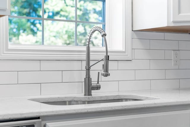 interior details with dishwashing machine, white cabinetry, tasteful backsplash, sink, and light stone counters