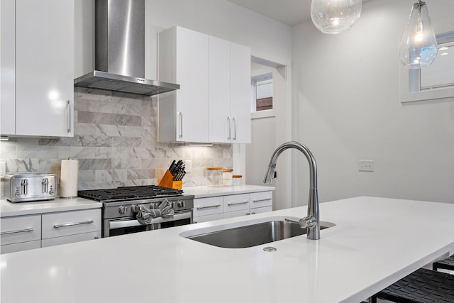 kitchen with sink, stainless steel gas stove, white cabinets, and wall chimney range hood