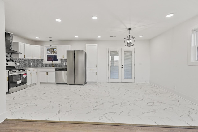 kitchen featuring appliances with stainless steel finishes, wall chimney exhaust hood, decorative light fixtures, white cabinetry, and french doors