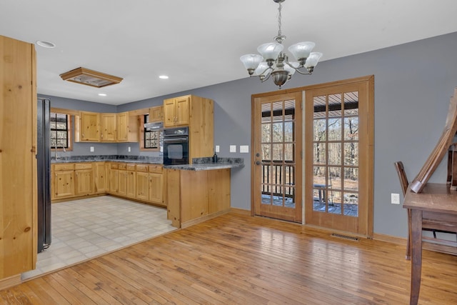 kitchen with black oven, hanging light fixtures, a notable chandelier, light brown cabinets, and light wood-type flooring