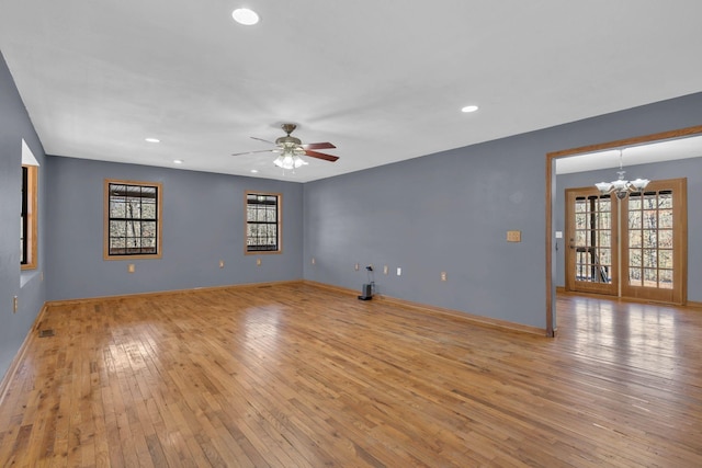 empty room featuring ceiling fan with notable chandelier and light wood-type flooring