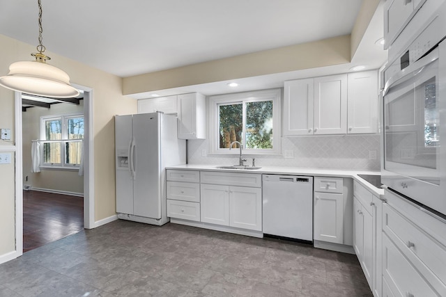 kitchen with white appliances, pendant lighting, white cabinetry, decorative backsplash, and sink