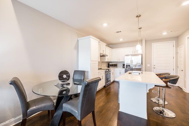 kitchen featuring sink, white cabinetry, hanging light fixtures, appliances with stainless steel finishes, and an island with sink