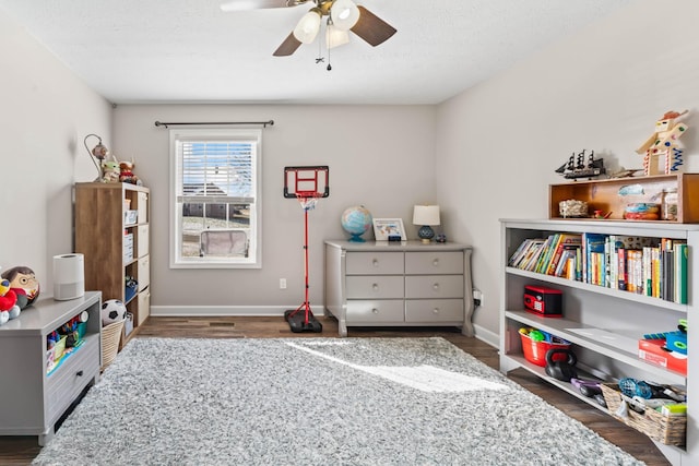 recreation room featuring dark wood-type flooring, a textured ceiling, and ceiling fan